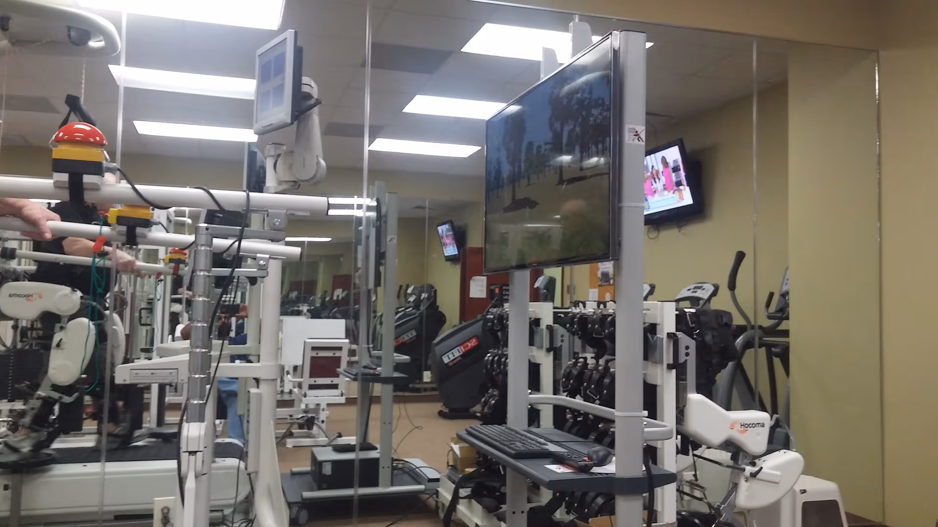 Interior gym area with treadmills, weight machines, and wall-mounted screens.
