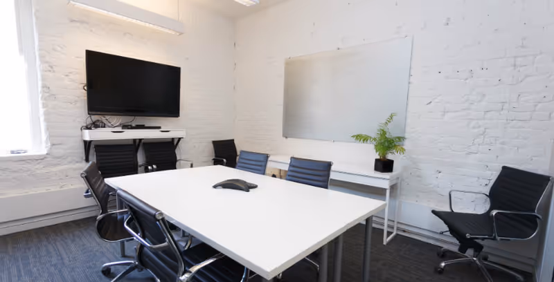 A modern conference room with a long white table, black chairs, and wall-mounted TV.