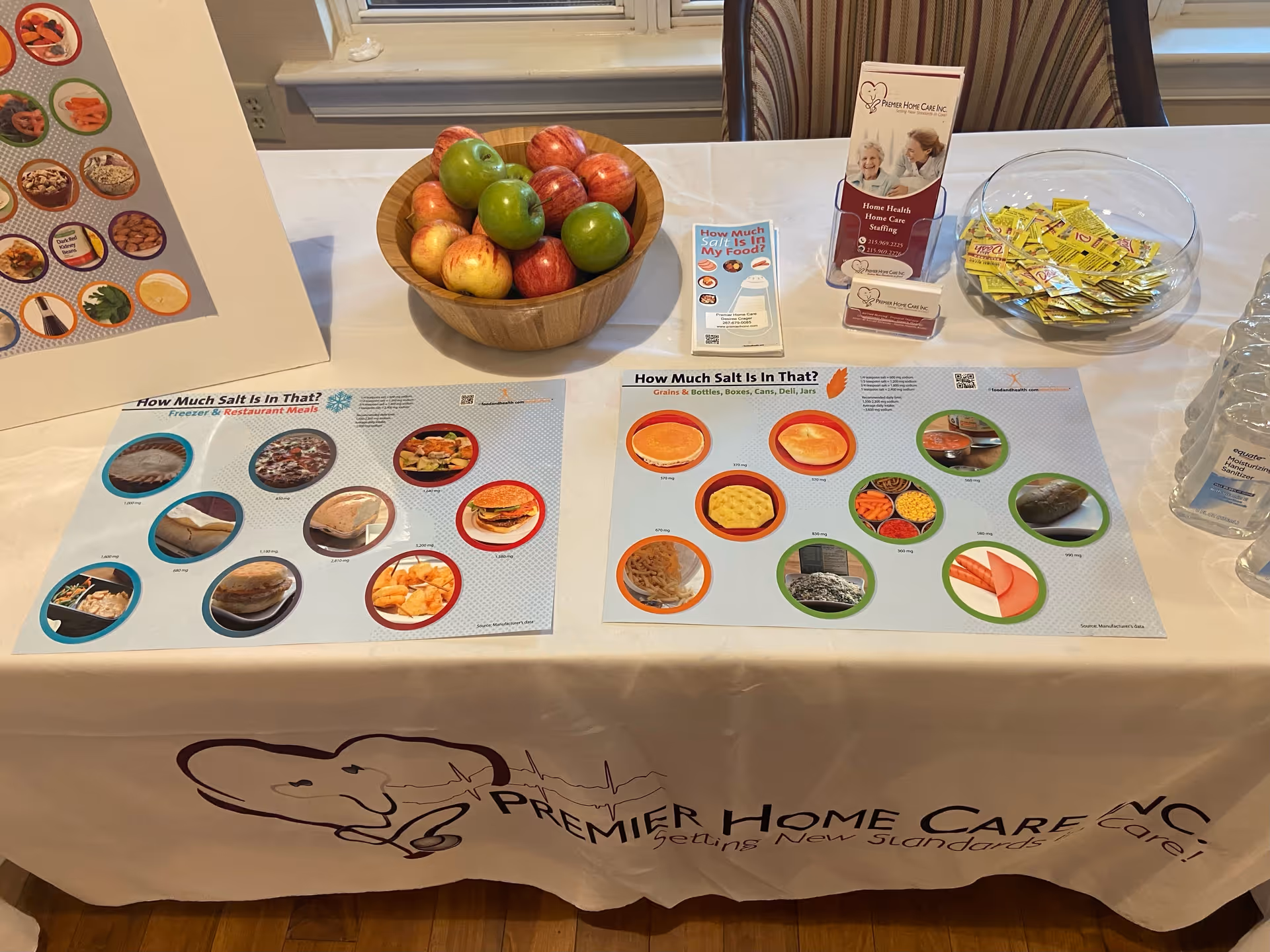 Table display with apples, brochures, and Premier Home Care banner in an indoor facility.
