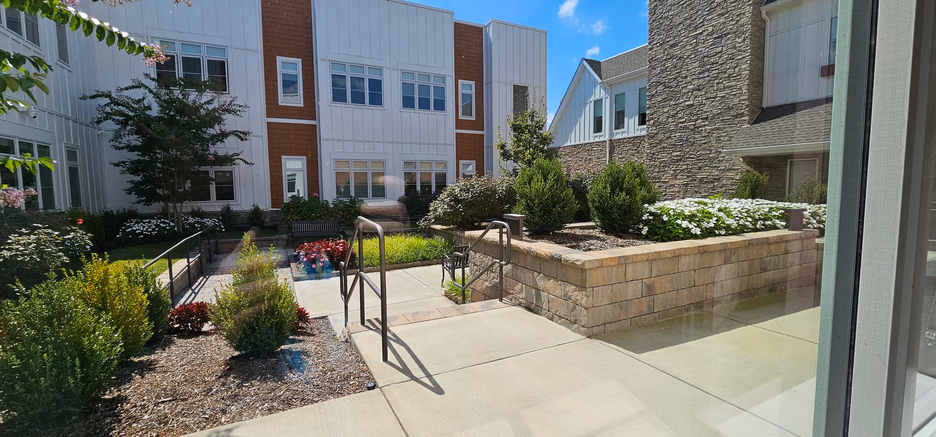 Outdoor courtyard at a senior living facility with ramps, stairs, and planters.