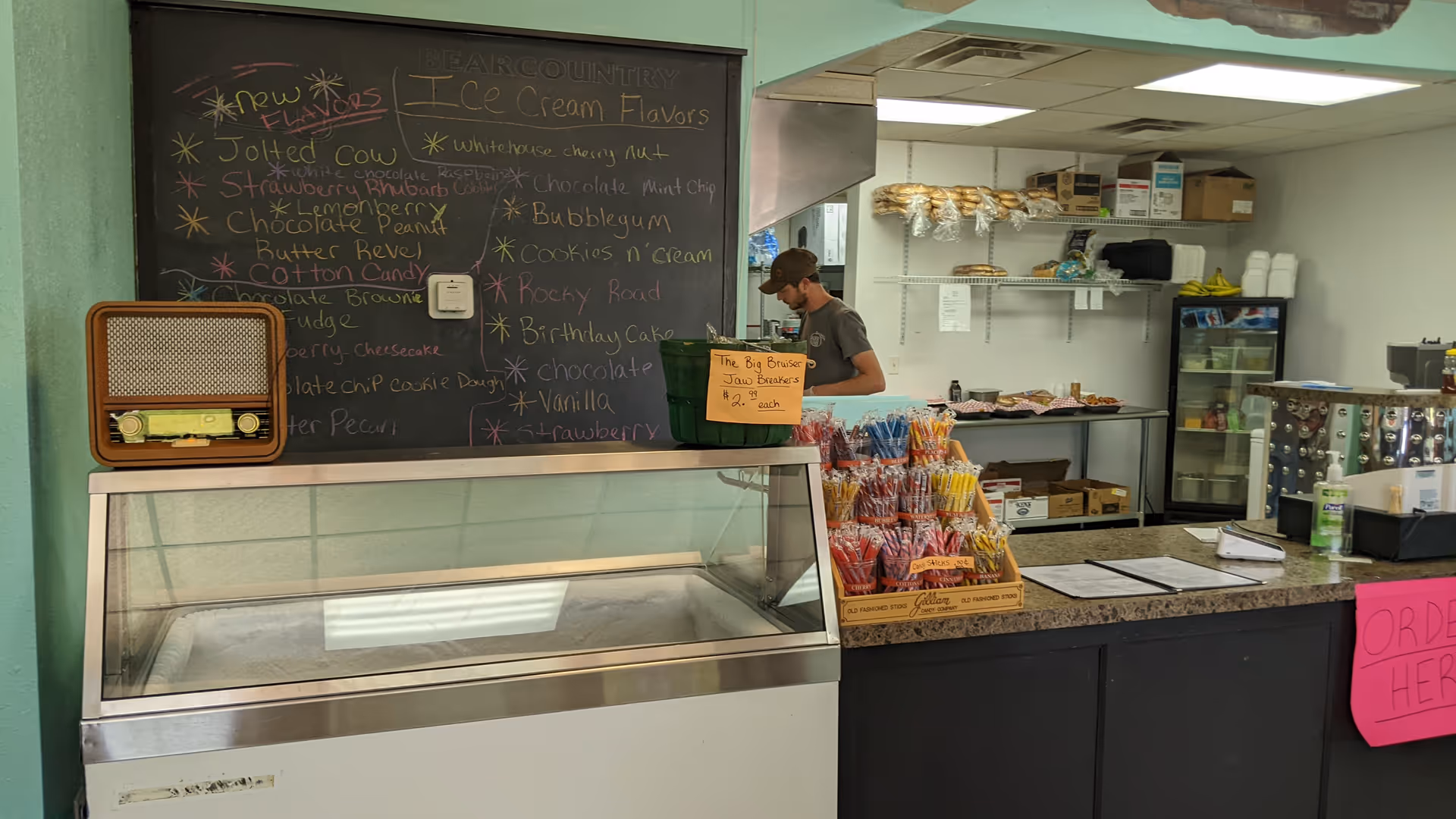 Staff member behind a cafe counter with a chalkboard menu inside a senior living facility.