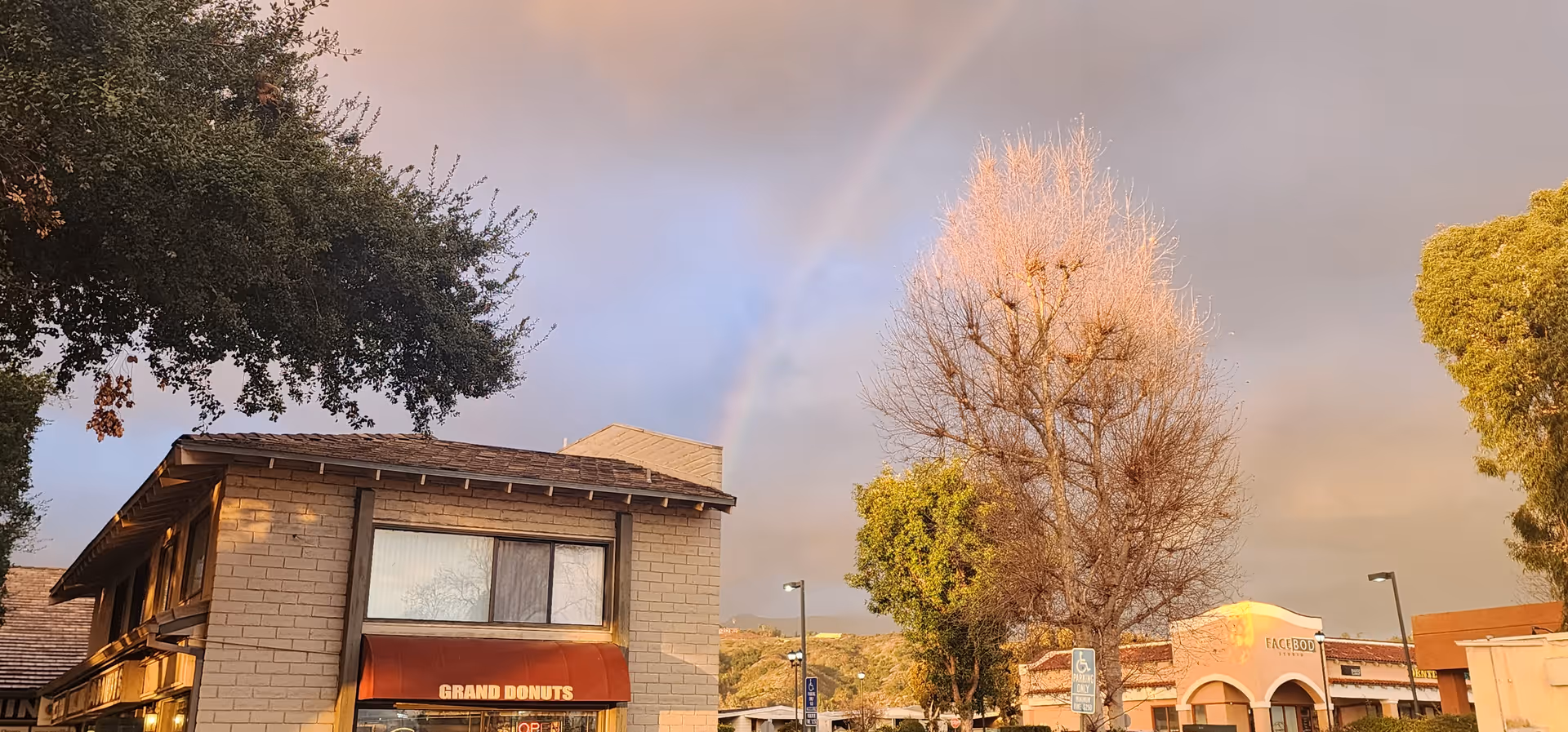 Street view of a brick storefront with a red awning and a rainbow in the sky.