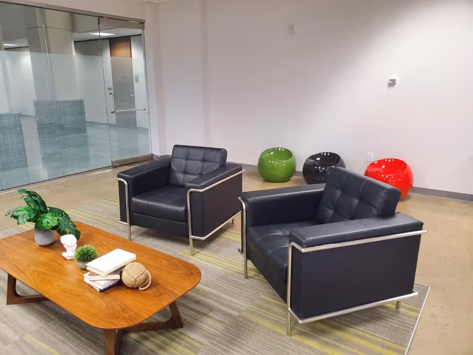 Interior lounge with black leather chairs, a wooden coffee table, and colorful round seats.