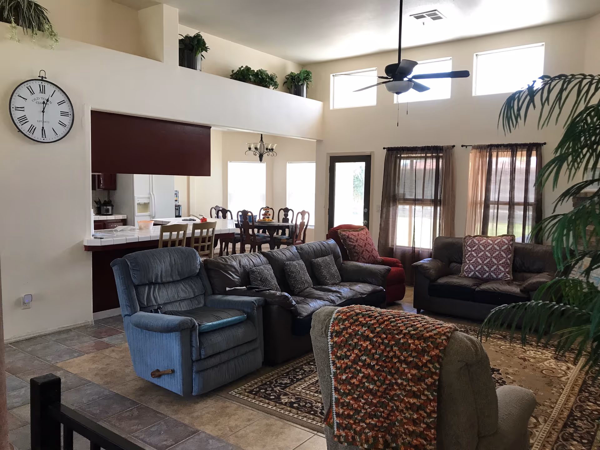 Bright senior living lounge with sofas, a dining area, and potted plants.