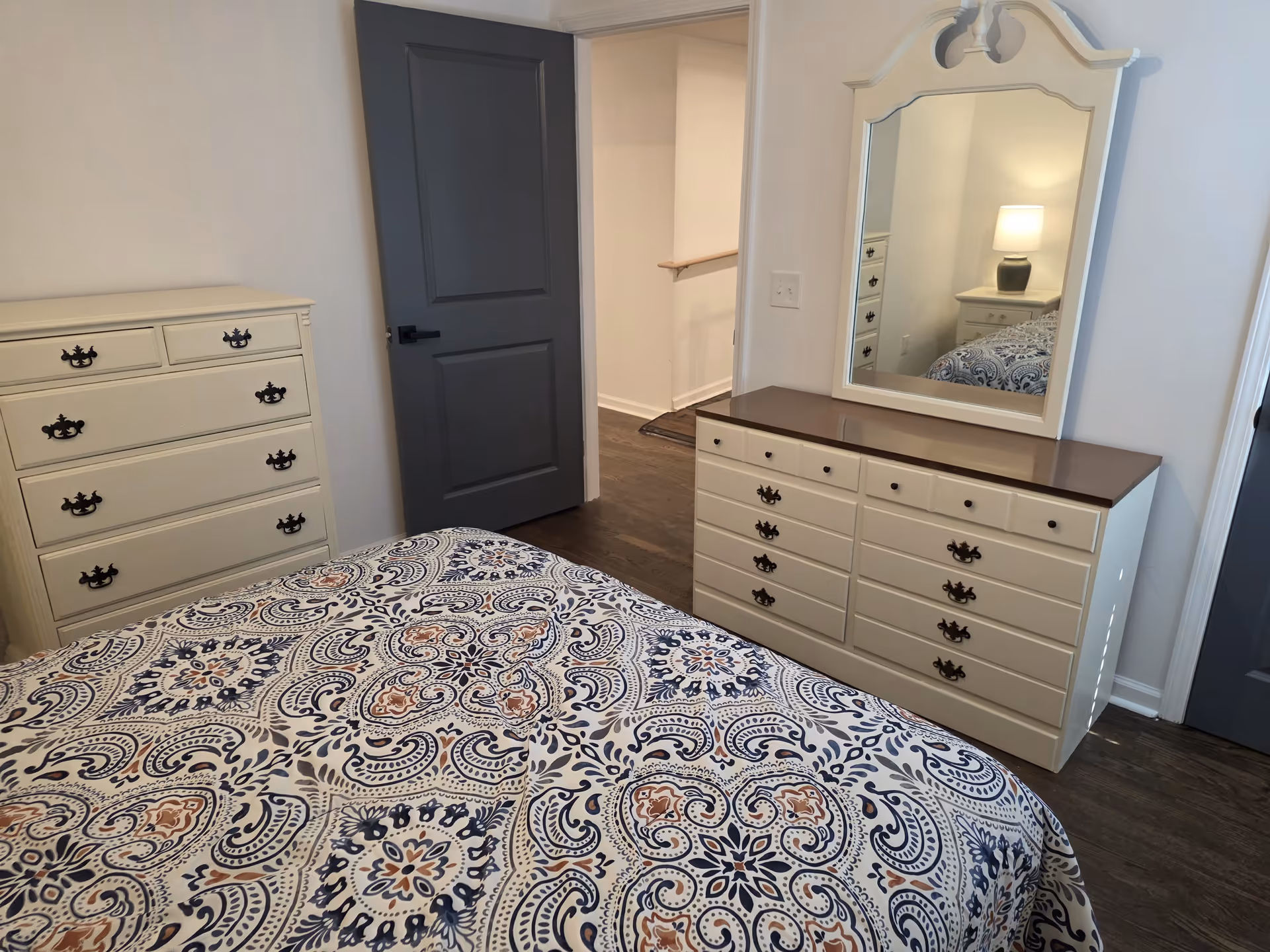 Bedroom in a senior living facility featuring matching cream dressers, mirror, and bedspread.