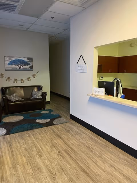A small interior lobby with a sofa, wall art, patterned rug, and reception window.