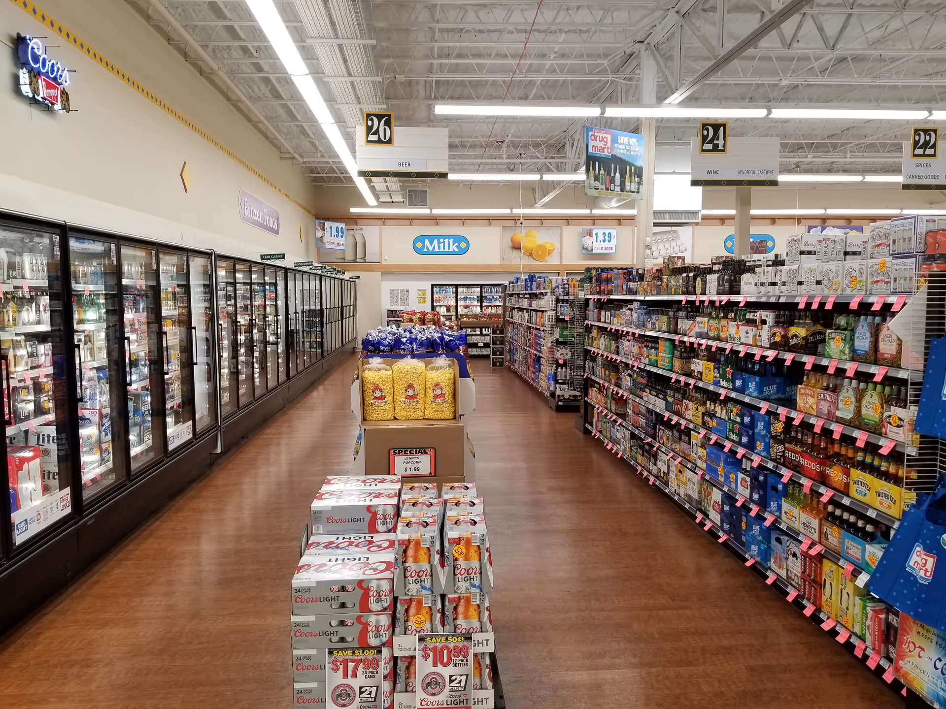 Indoor store aisle with refrigerated section on the left and shelves on the right.