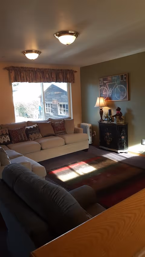 Cozy living room featuring a beige sectional, window, rug, and decorative cabinet.