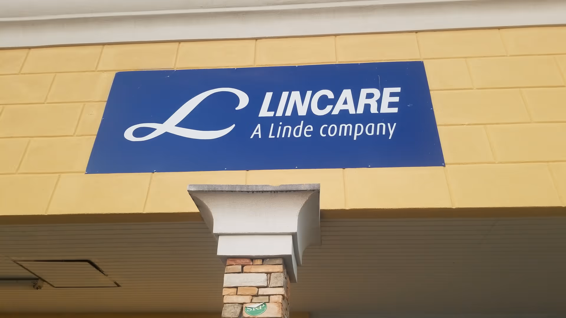 Blue LINCARE sign on a yellow exterior wall reading Lincare A Linde company.