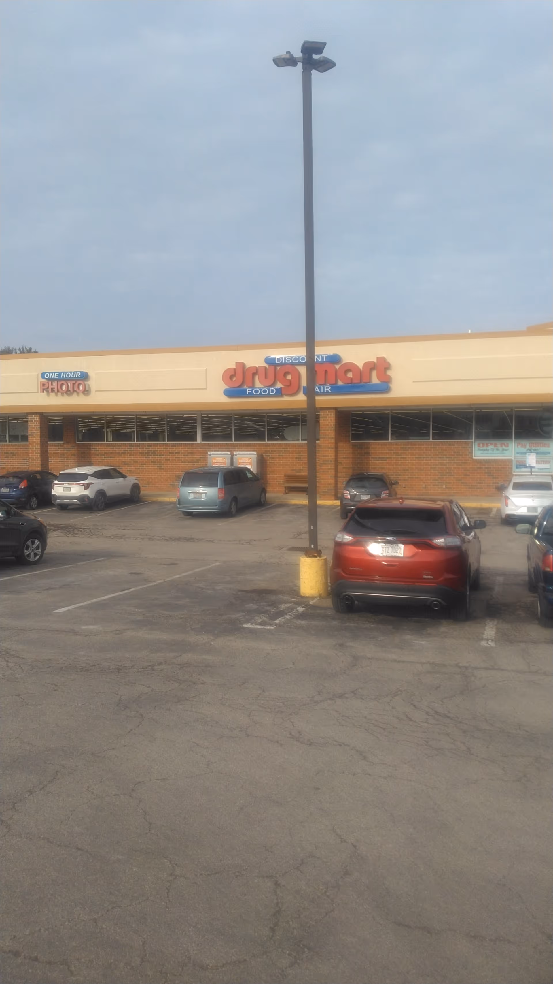 Parking lot in front of Discount Drug Mart with several cars parked.