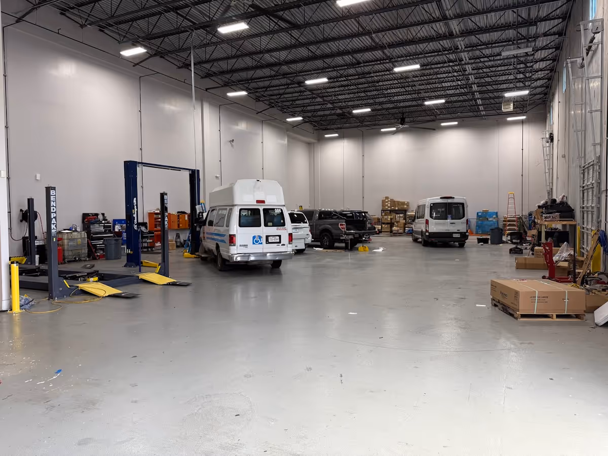 A large indoor workshop with multiple vans, a vehicle lift, and scattered equipment.
