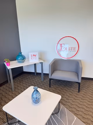 Cozy lounge corner in Elite Care At Home with gray chair, white table, and vases.