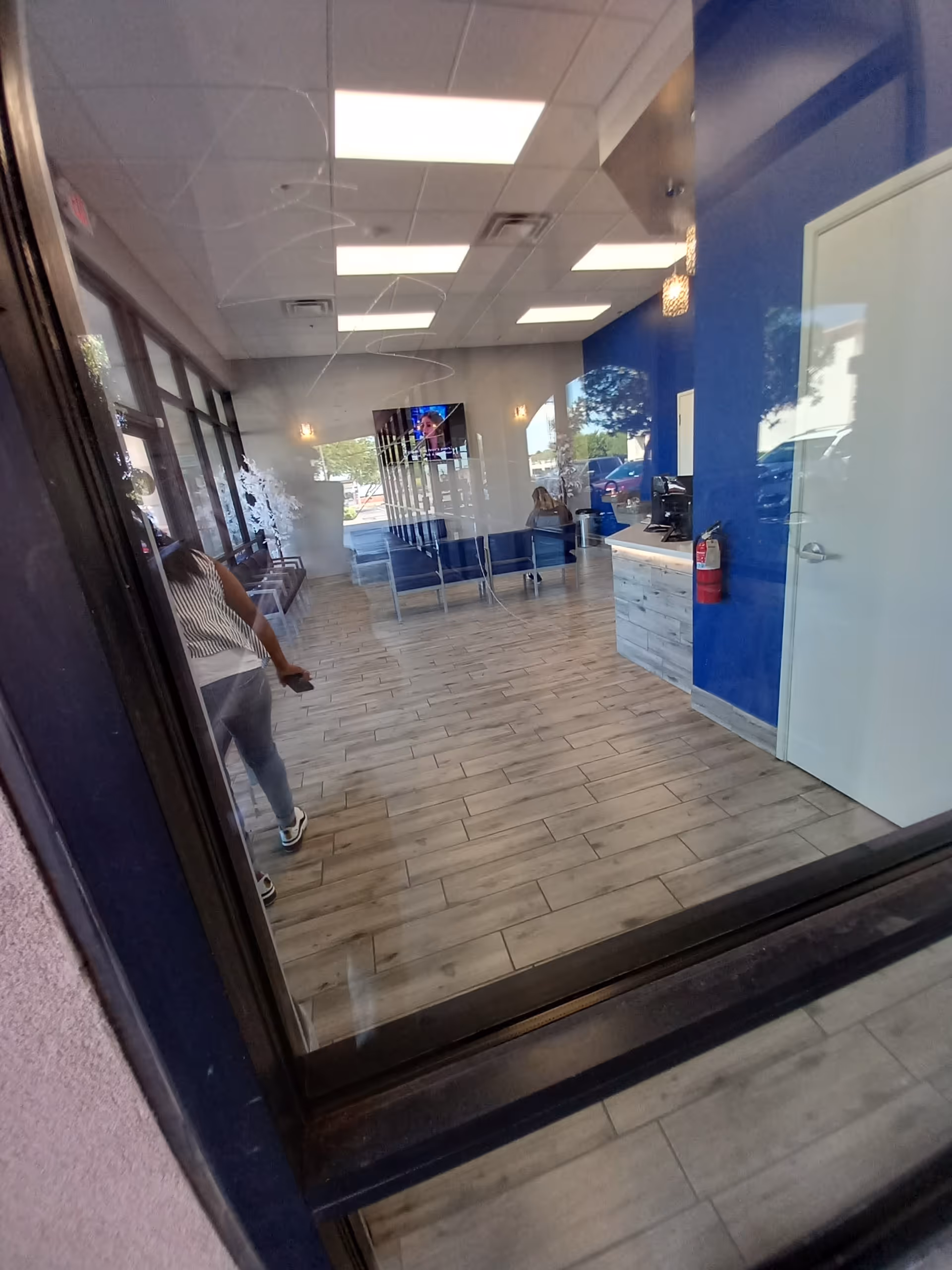 Blue-walled lobby with reception desk, seating, and windows; person passing by.