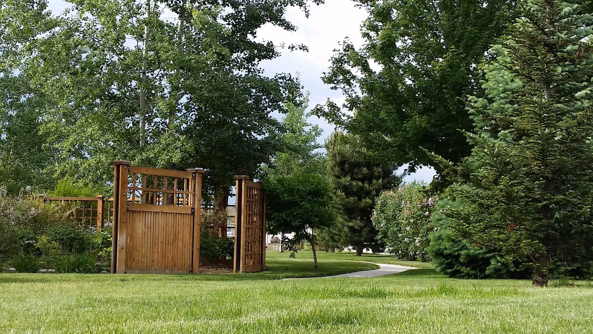 Two wooden gates, lush lawn, and trees mark the outdoor entrance of a senior living campus.