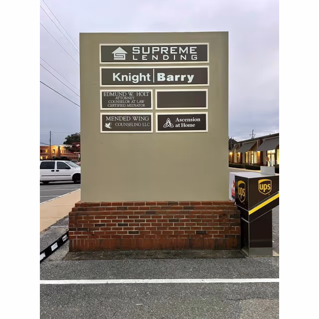 Large outdoor sign with multiple business panels and a brick base in a parking lot.