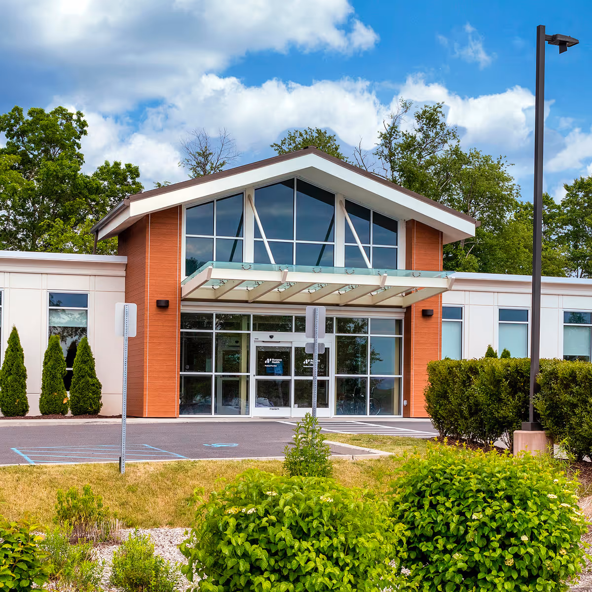 Modern medical center entrance with glass doors, landscaped front, and blue sky.