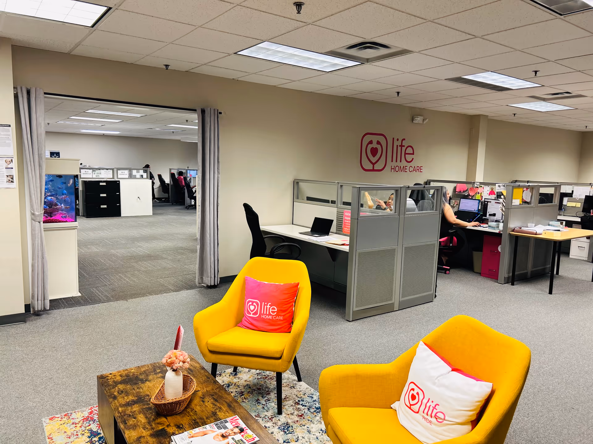 Open office area with cubicles, yellow chairs, and a Life Home Care sign on the wall.