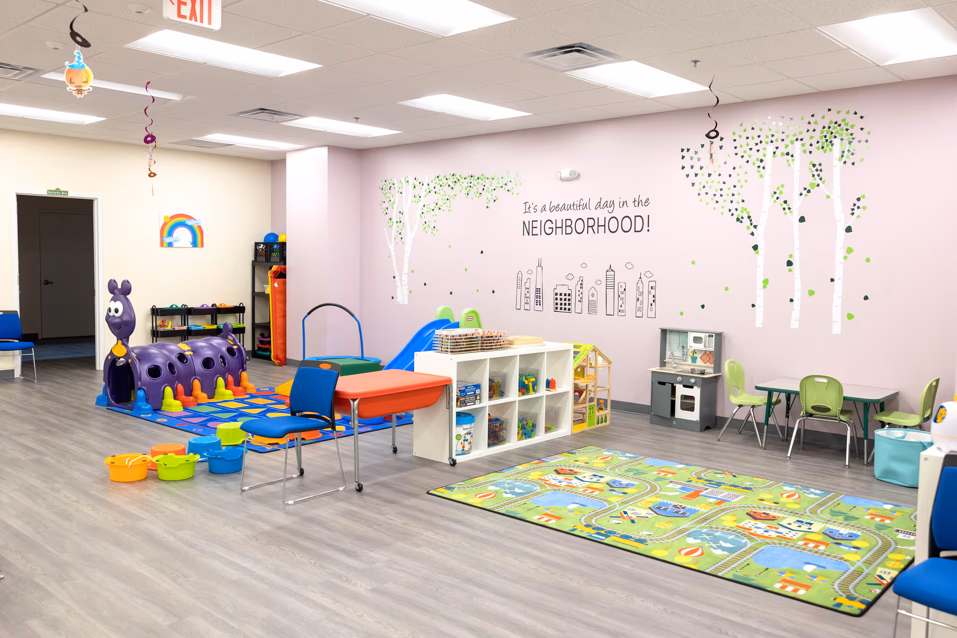 Bright indoor children's play area with toys, mats, and pastel wall mural inside a facility.