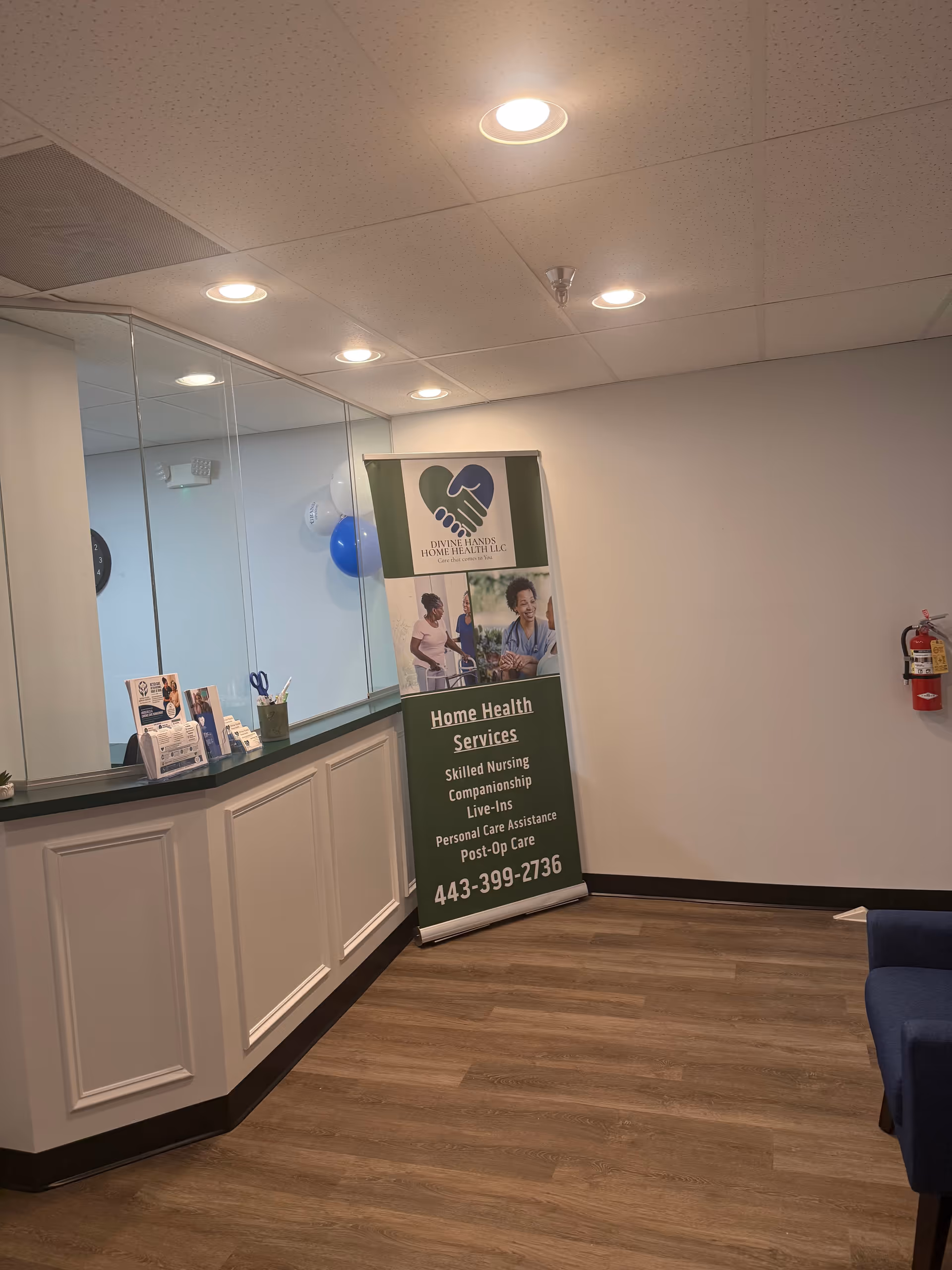 Reception area with a Divine Hands Home Health LLC banner, glass partition, and wooden floor.