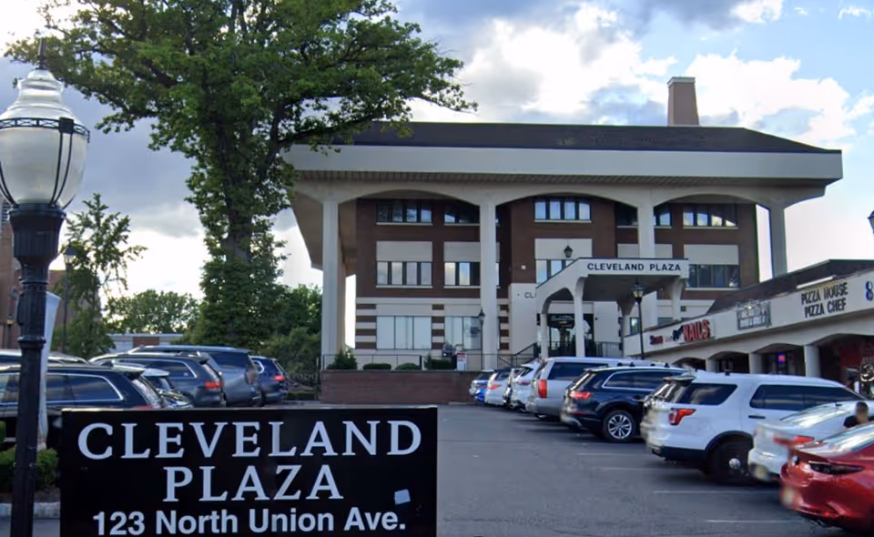 Exterior view of Cleveland Plaza shopping center with parked cars in front.