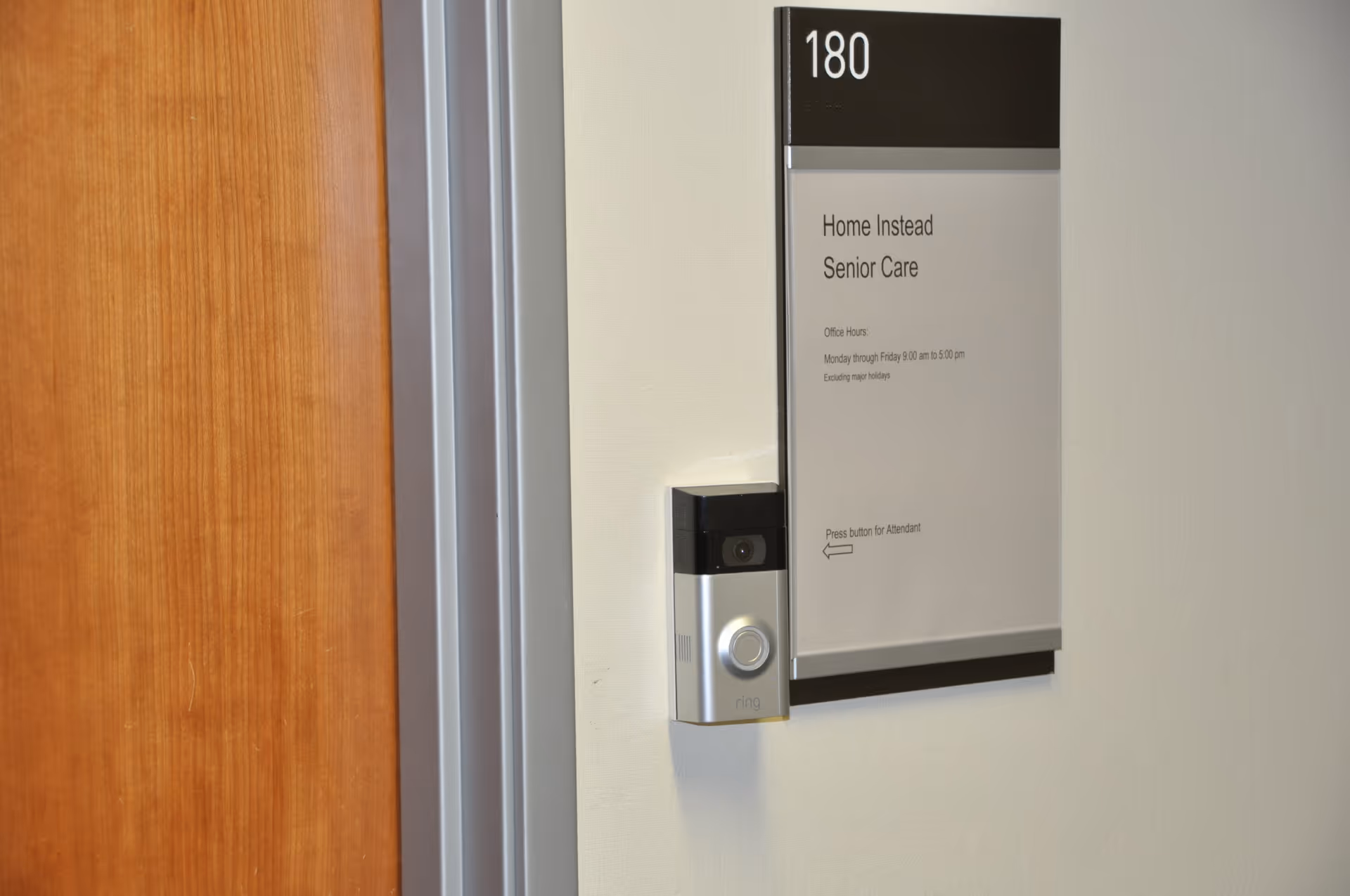 Interior wall with room sign 'Home Instead Senior Care' and doorbell intercom near doorway.
