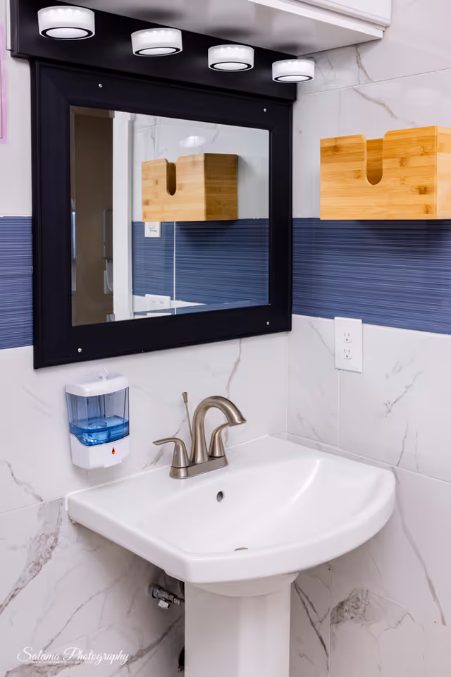 Bathroom sink with faucet, mirror, soap dispenser, and bright vanity lights.