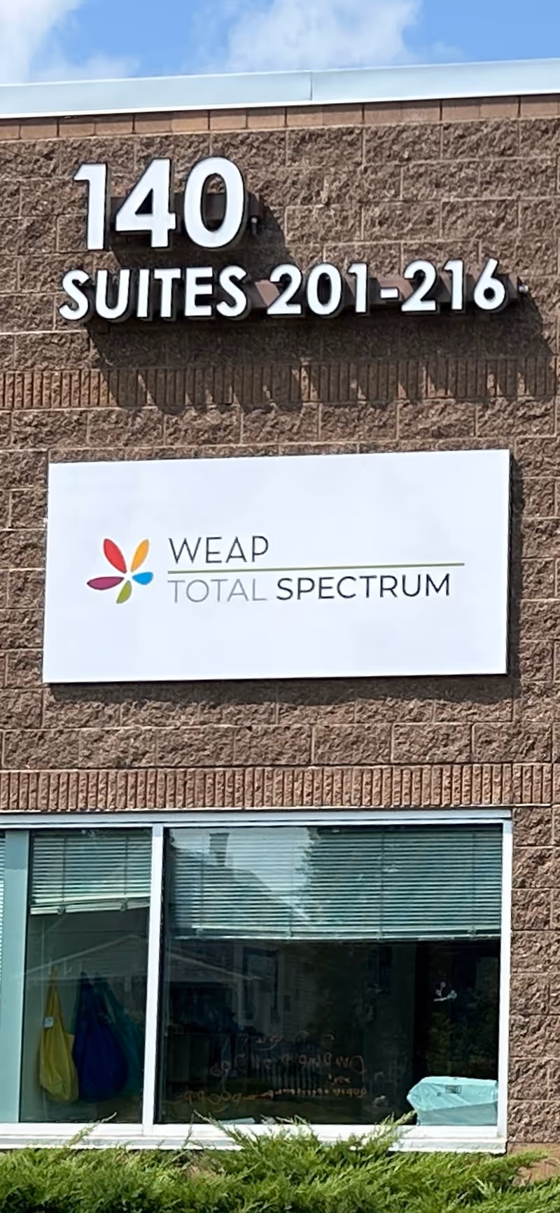 Brick exterior of a facility with 140 Suites 201-216 and WEAP TOTAL SPECTRUM sign.