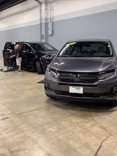 A technician stands beside a black SUV in a service facility beside a gray Honda van.