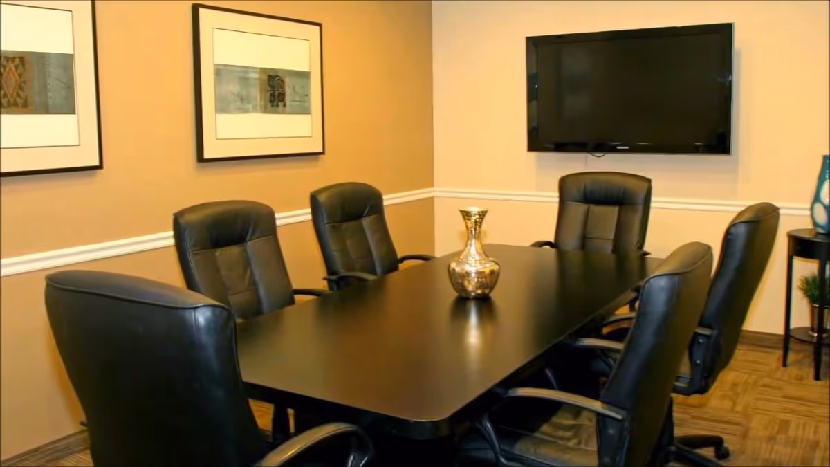 A long dark conference table with black leather chairs in a beige meeting room.