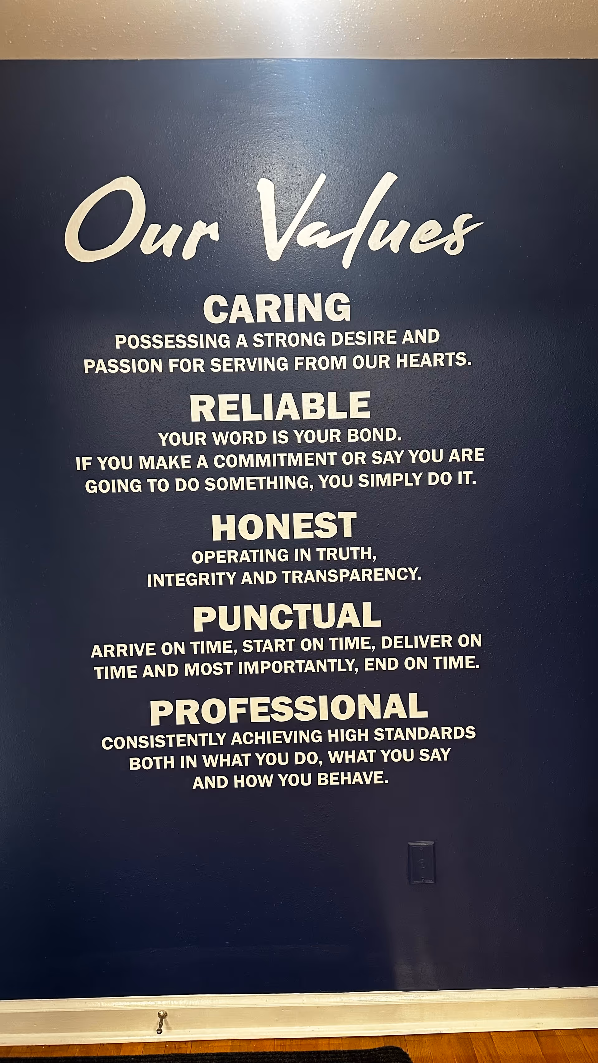 Dark blue wall with a white 'Our Values' sign listing core traits.