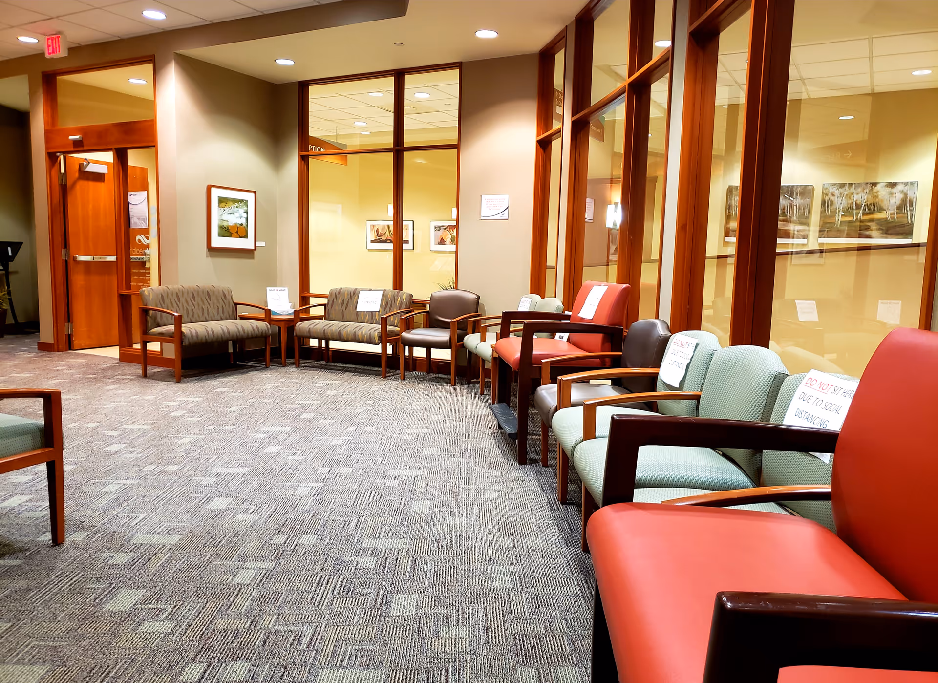 Lobby waiting area with upholstered chairs and glass-walled offices in an outpatient center.