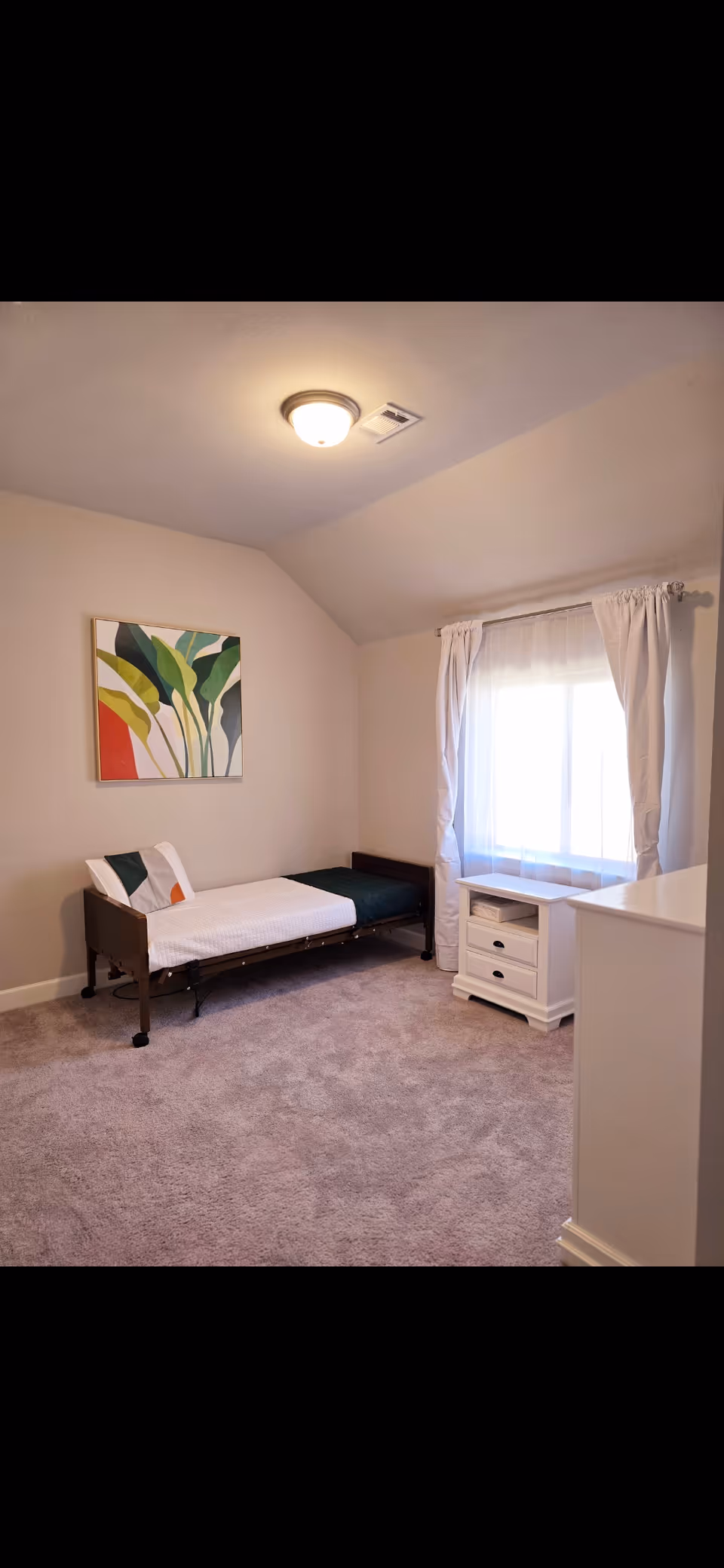 A small, tidy bedroom with a single bed, white furniture, and a window with curtains.