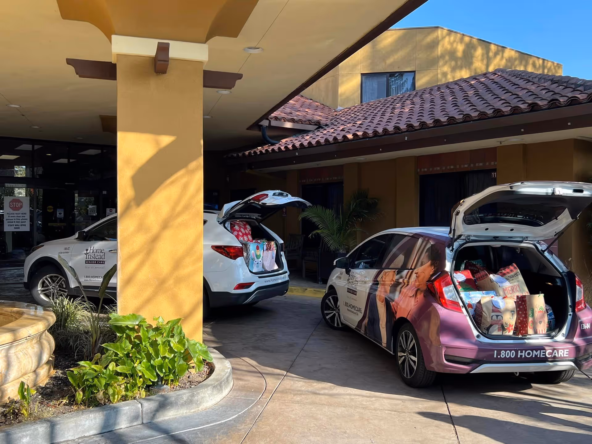 Front entrance of a tan building with two Home Instead vehicles and open trunks.