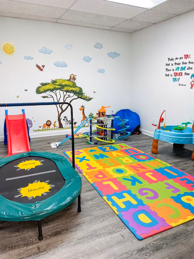 Colorful indoor playroom with alphabet mats, a trampoline, and a wall mural.