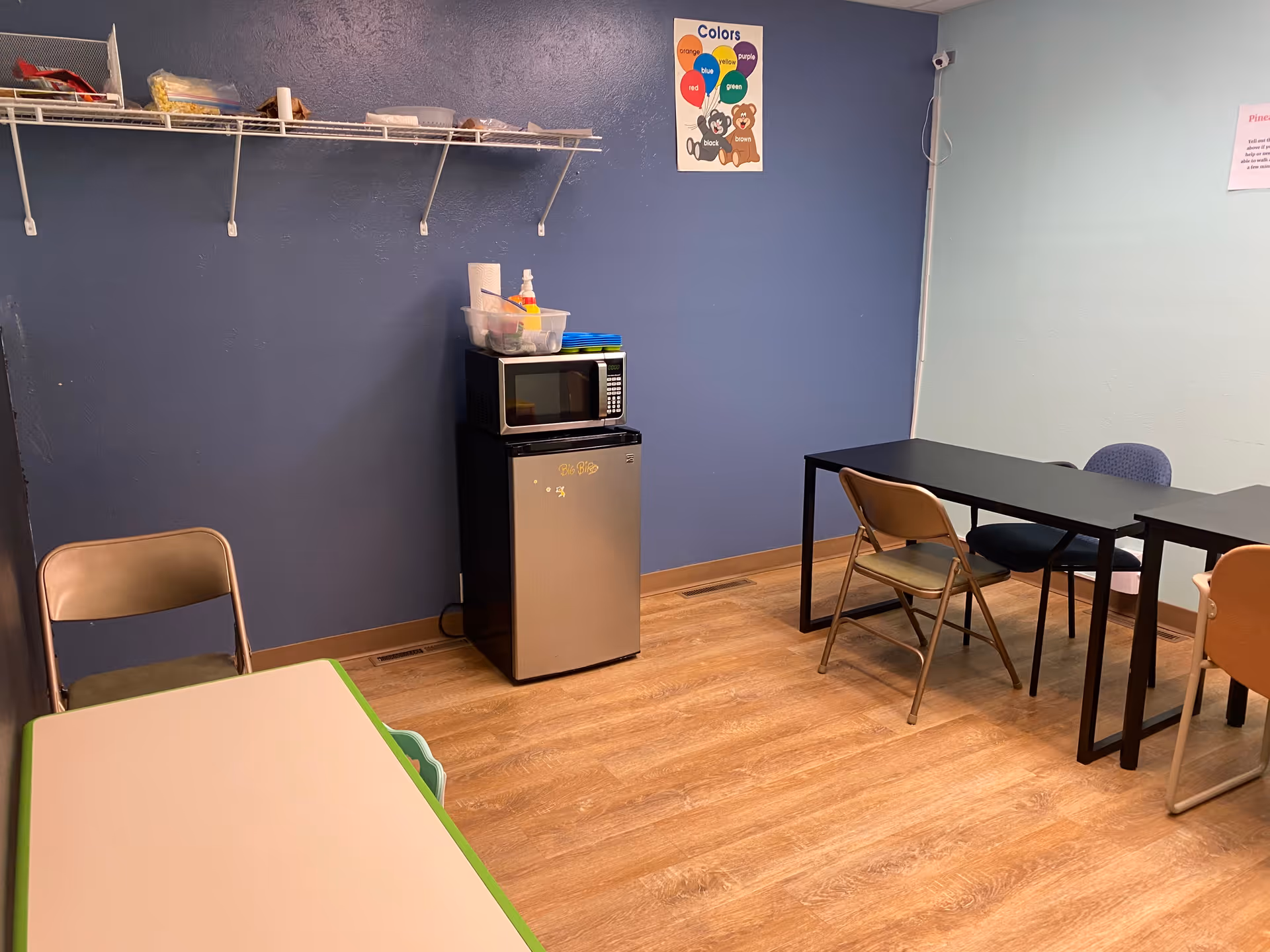 A small kitchen and dining area with a microwave, mini-fridge, and tables.
