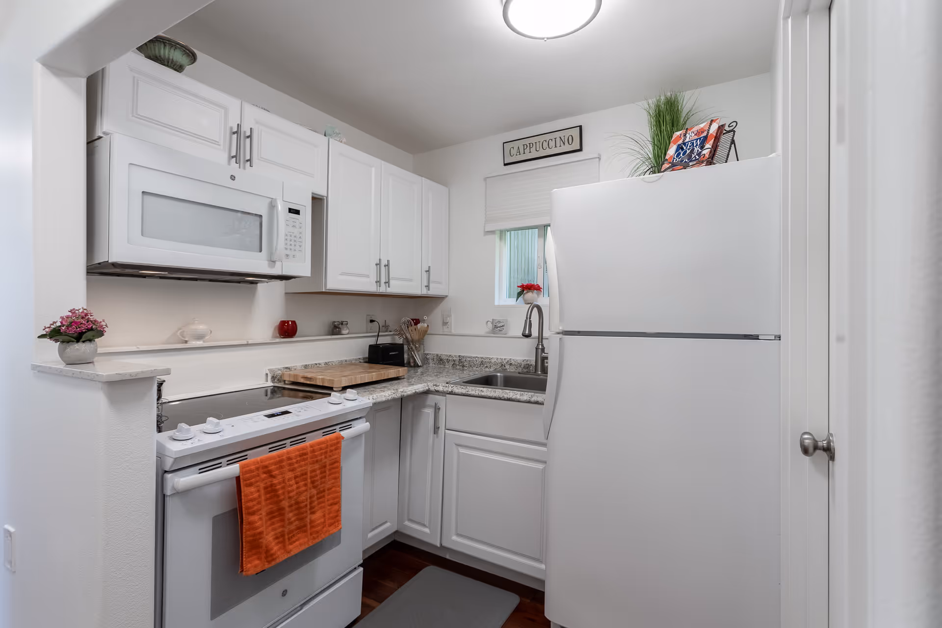 Compact white kitchen with stove, microwave, sink, and fridge.