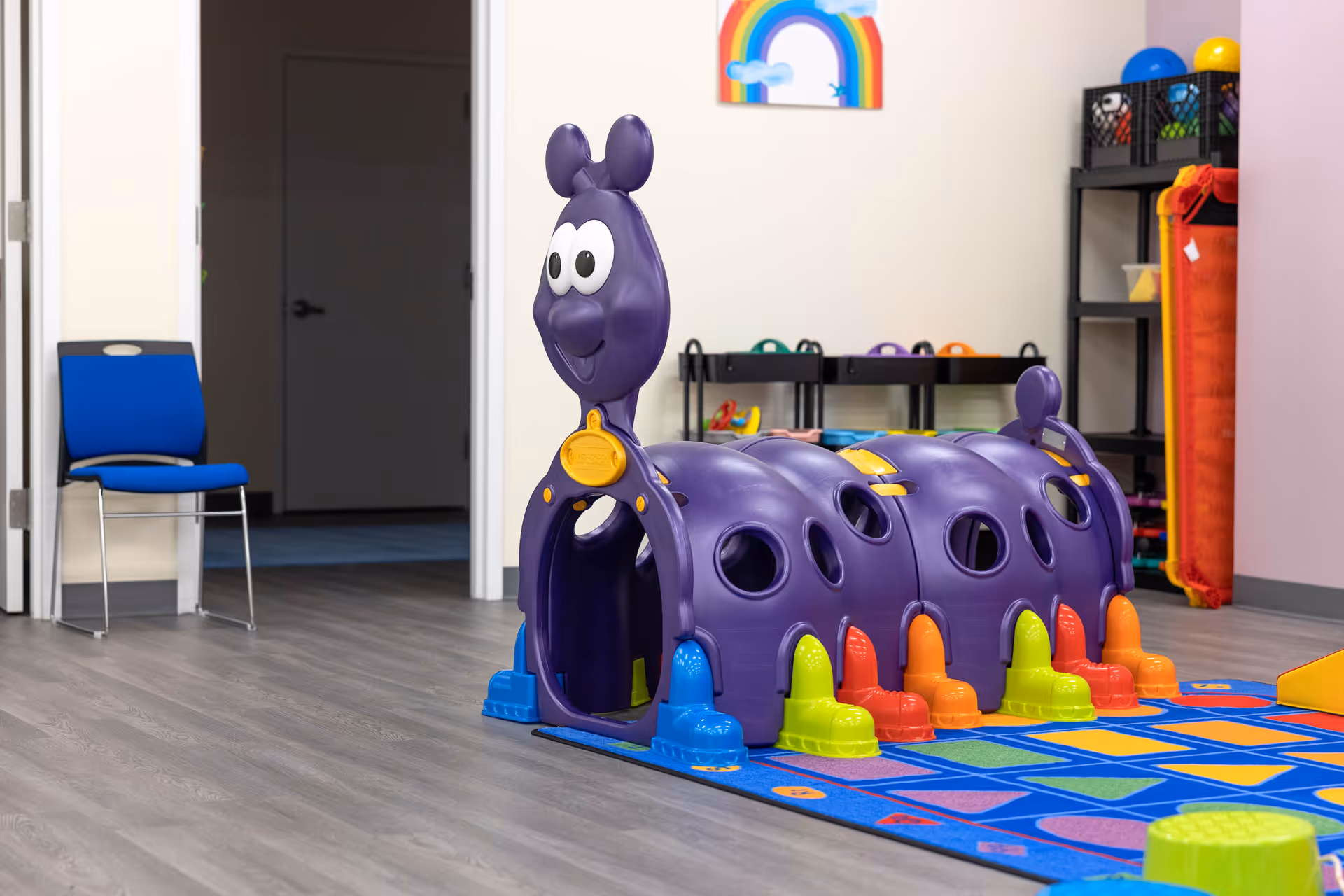 Indoor playroom with a purple caterpillar toy, colorful rug, and shelving.