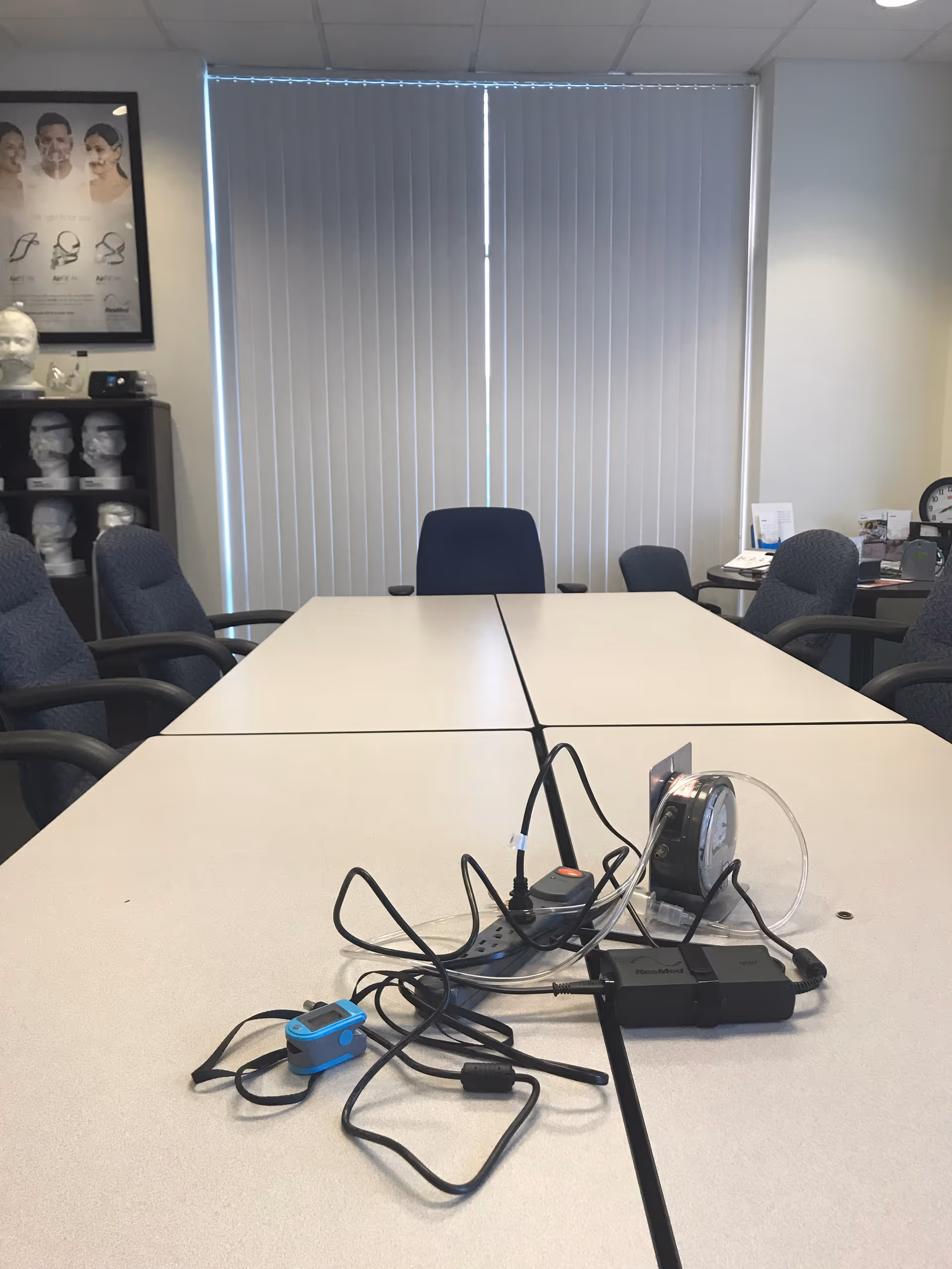 A conference room table with cables and medical equipment, surrounded by blue chairs.
