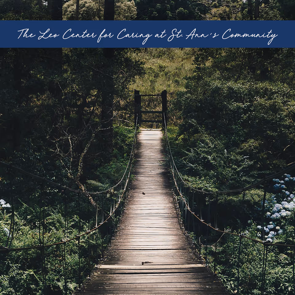 Wooden suspension bridge spans lush greenery on the Leo Center for Caring grounds.