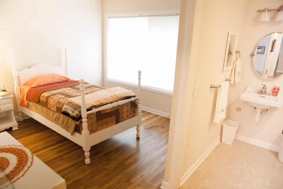 Bright bedroom with white four-poster bed and an adjacent bathroom.