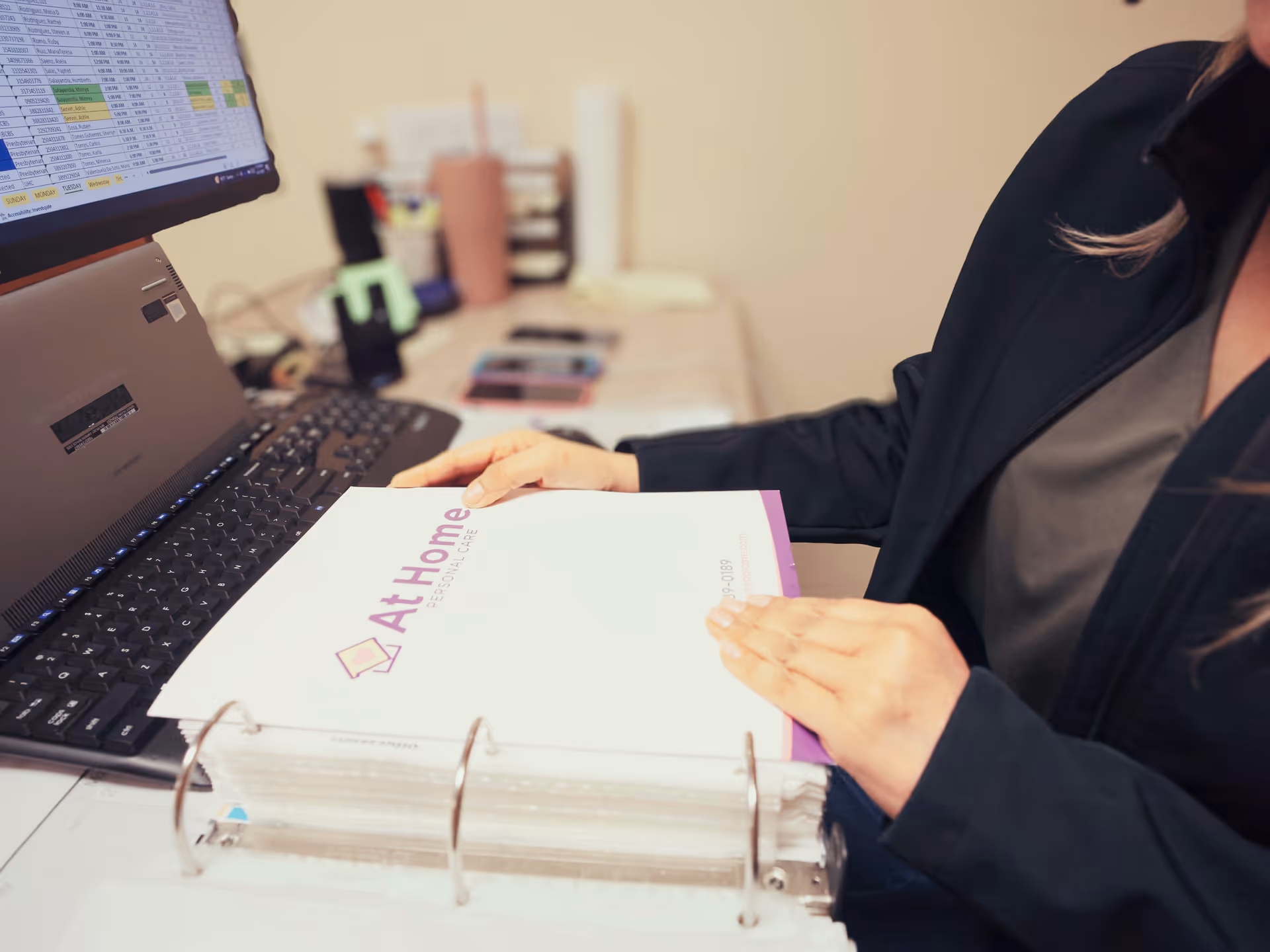 Office scene with a staff member at a desk reviewing an At Home binder.