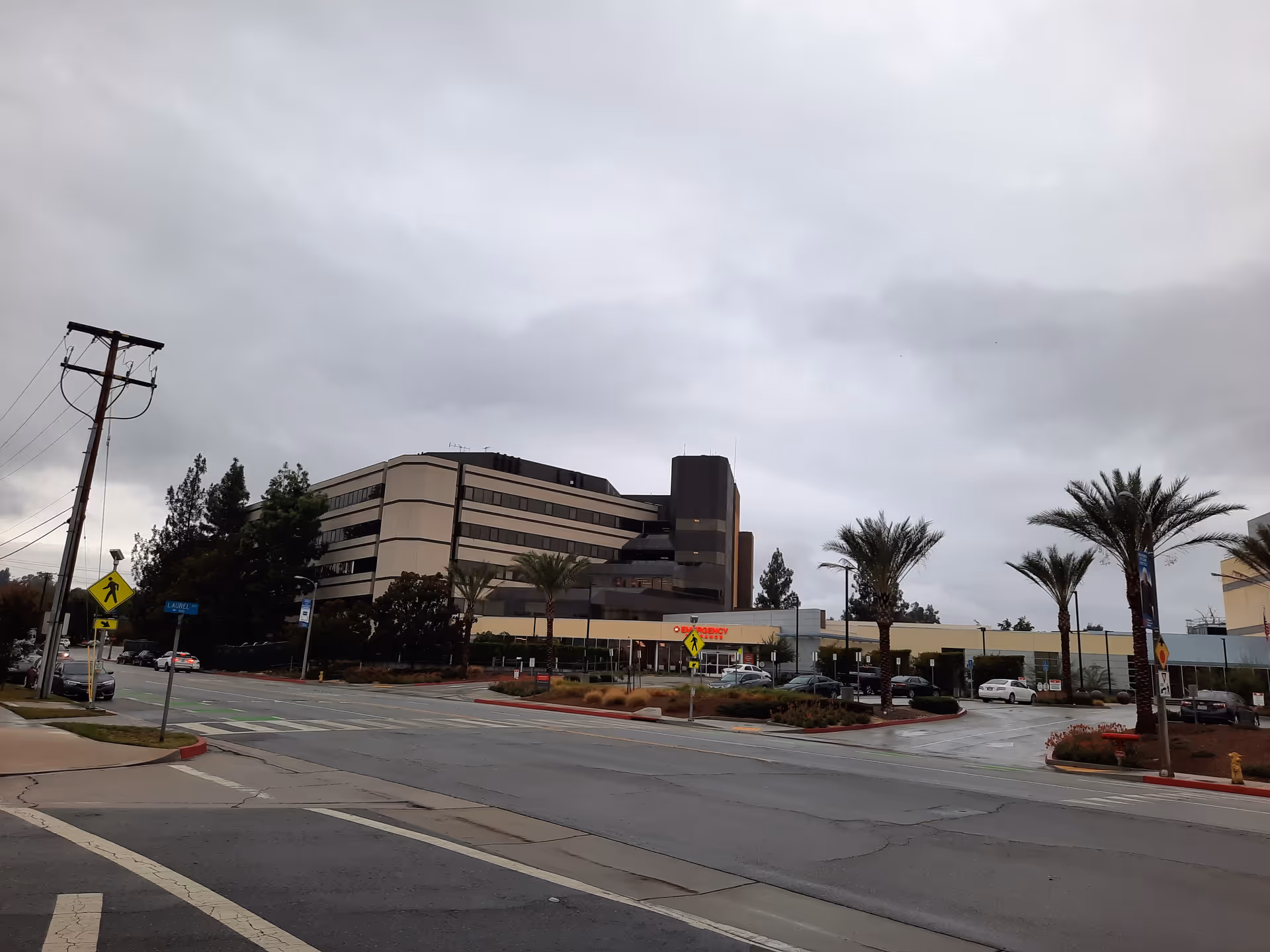 Wide street view of Redlands Community Hospital front with palm trees and parked cars.