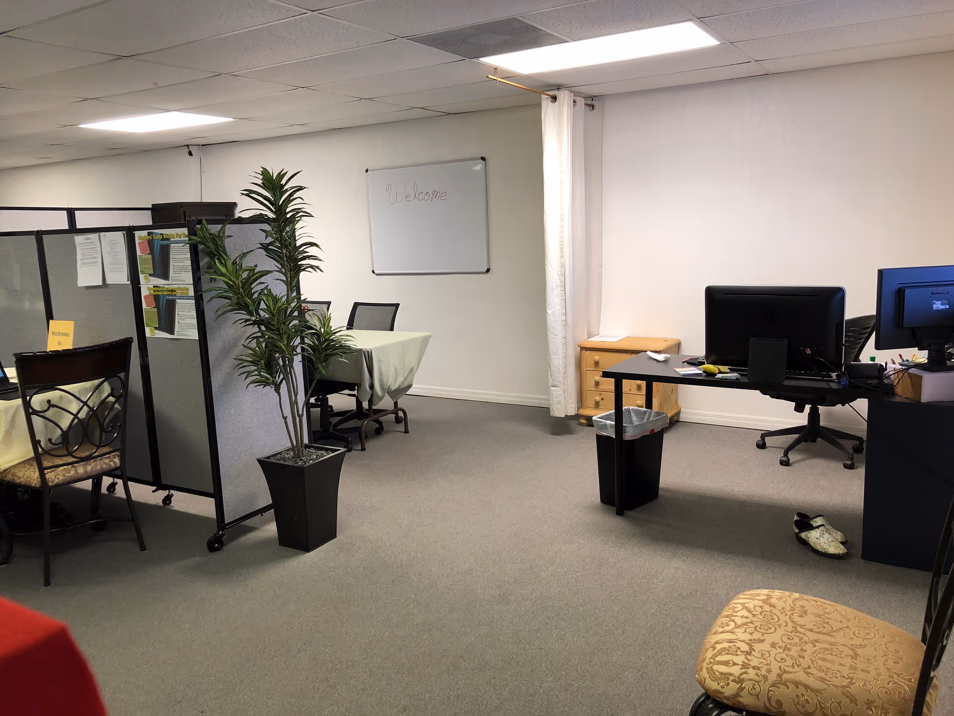 Office-like staff area with cubicles, desks, computers, a whiteboard, and potted plants.