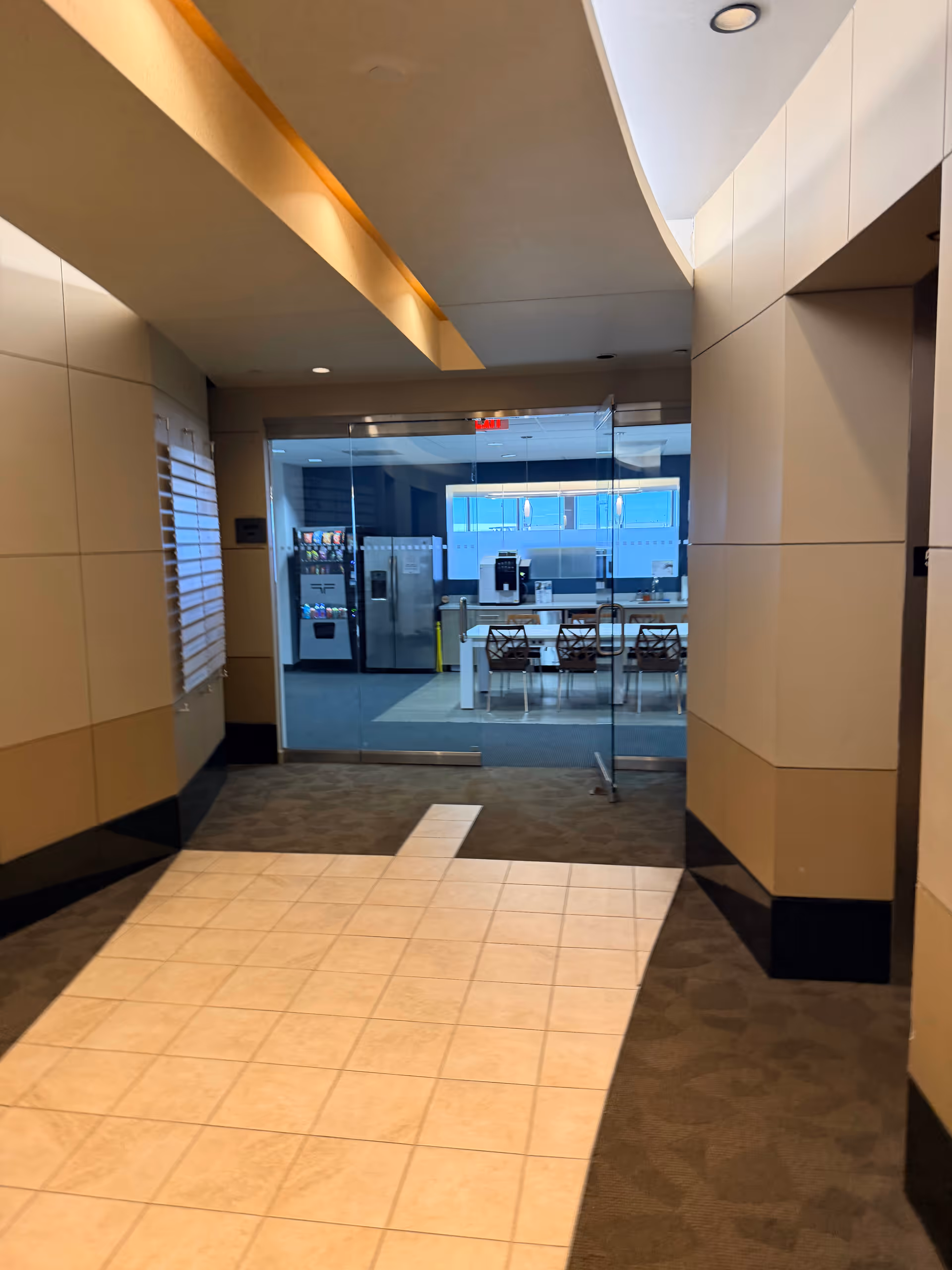 A hallway leads to a glass-walled room with vending machines and seating.