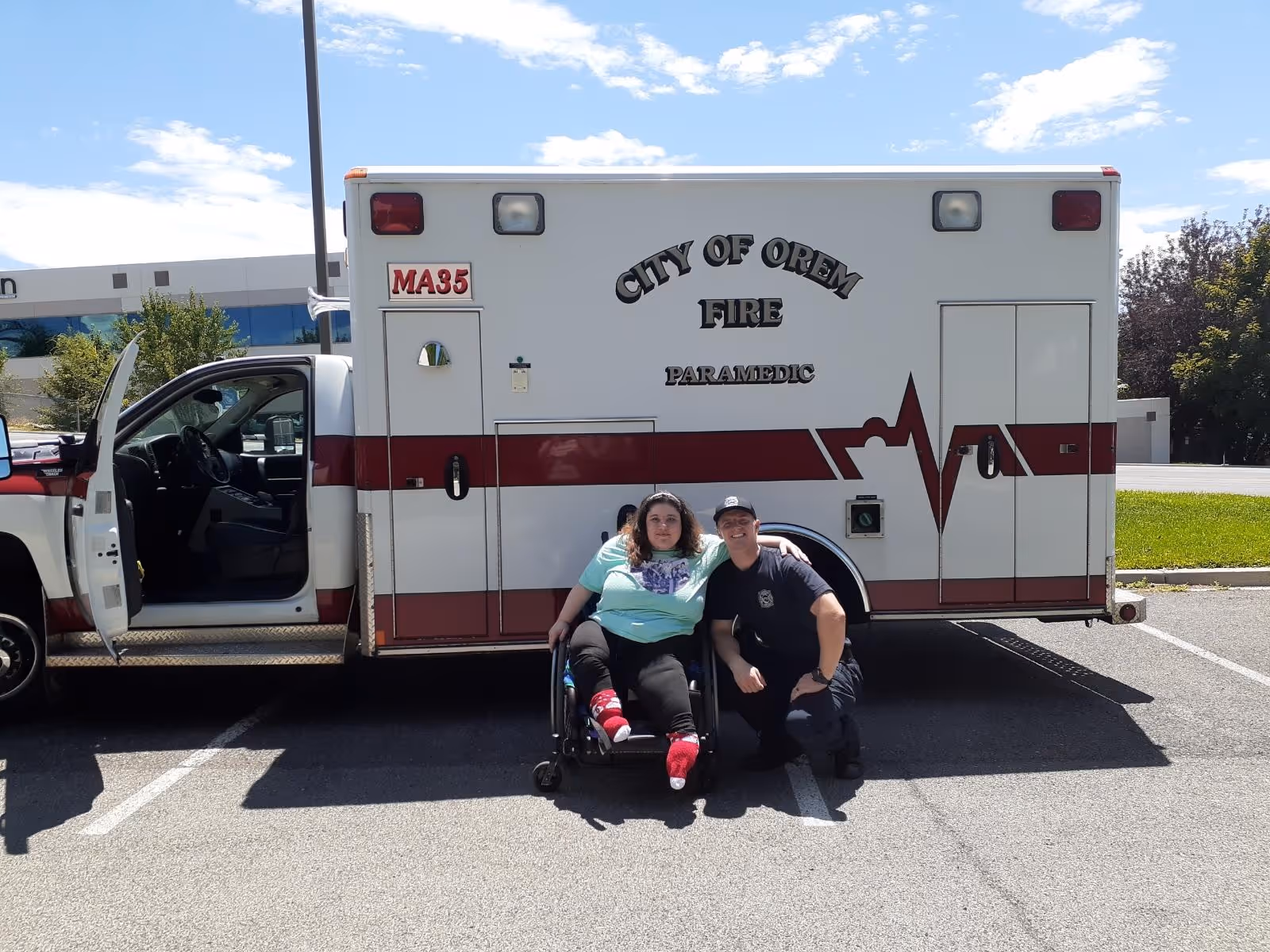 Two people sit beside a City of Orem Fire ambulance in a parking lot.
