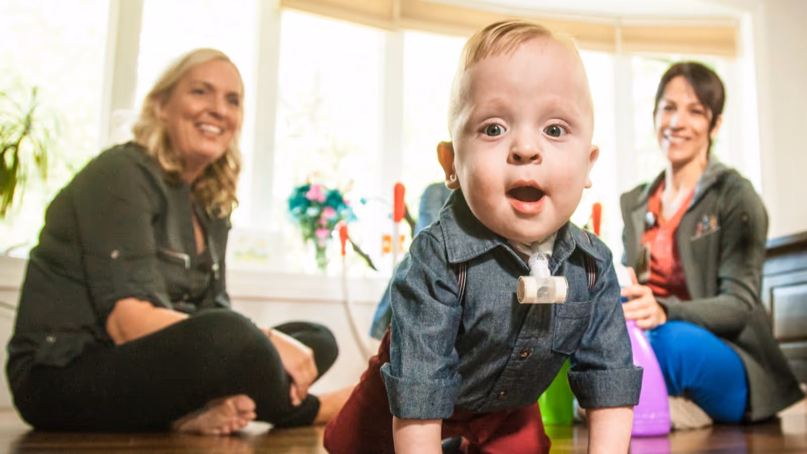 Crawling baby with two smiling caregivers in a bright room