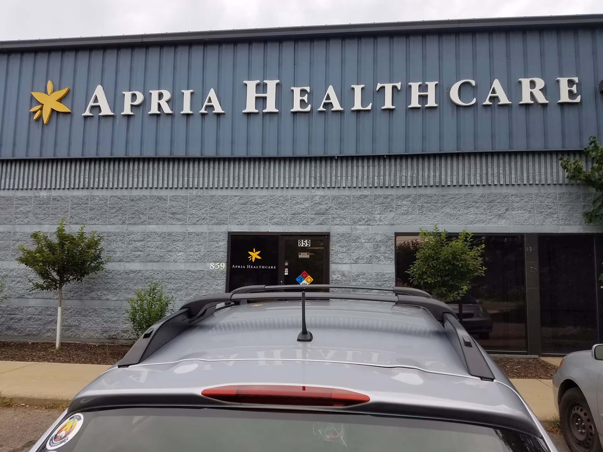Exterior view of Apria Healthcare building with parked cars in front.