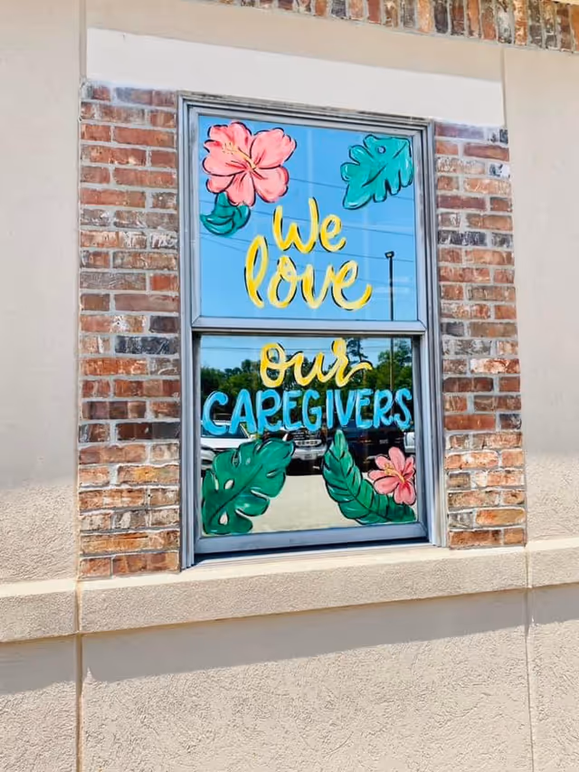 Exterior brick wall with a window displaying colorful We love our caregivers artwork.