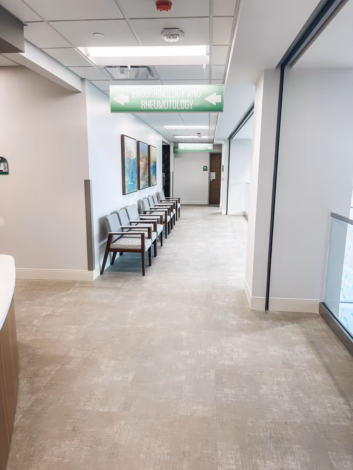 Long hallway in a healthcare facility with chairs along the wall and signs.
