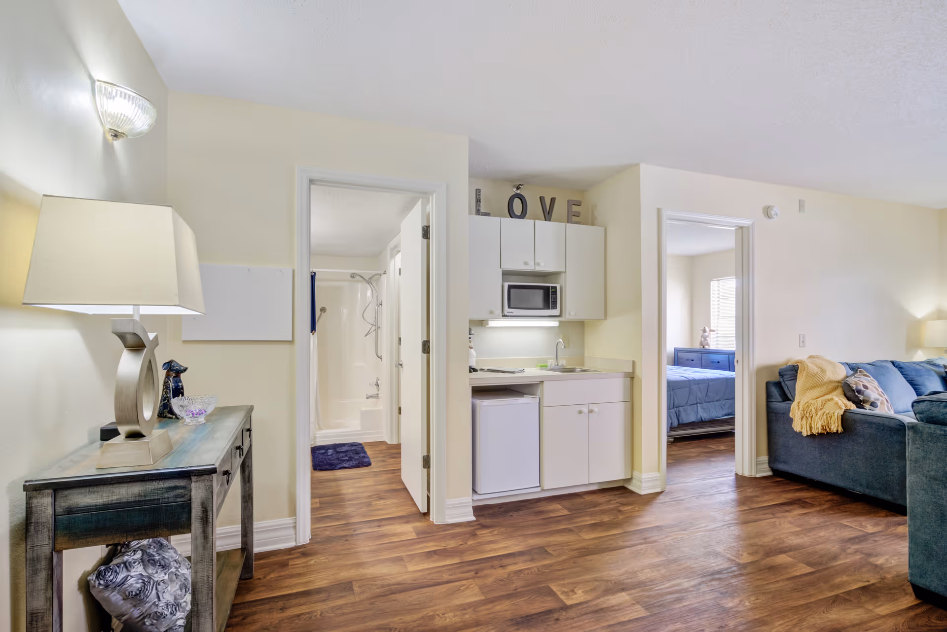 Interior of a senior living studio with kitchenette, couch, and bedroom visible.